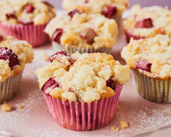 Saftige Rhabarber Muffins mit Streuseln, bestäubt mit Puderzucker. Ein Genuss für jeden Kaffeetisch.