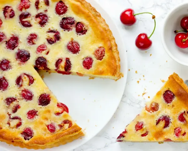 Ein köstlicher Pudding Kirsch Kuchen, mit frischen Kirschen belegt und goldbraun gebacken. Ein Stück wird gerade serviert.