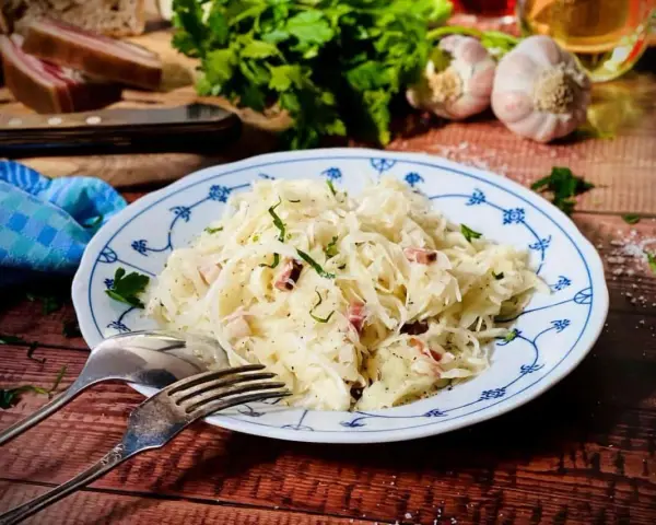Ein Teller mit Krautsalat, garniert mit Petersilie. Daneben liegen Gabel und Löffel. Ein leckeres Krautsalat Rezept für dich!