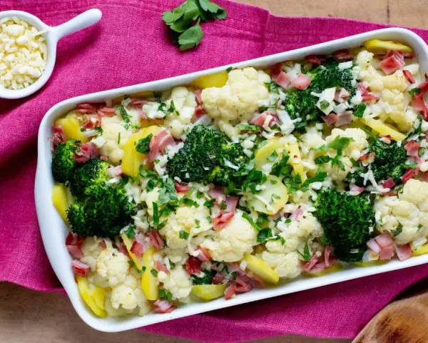Ein herzhafter Blumenkohl-Brokkoli-Auflauf mit Kartoffeln und Schinken, bestreut mit frischer Petersilie und Käse.