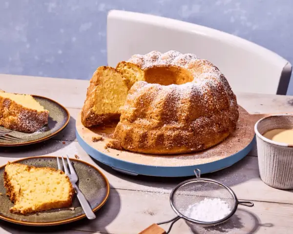 Ein goldbrauner Kartoffelkuchen mit Puderzucker bestreut, daneben zwei Teller mit Kuchenstücken, eine Tasse Kaffee und eine Kanne. Ein tolles Kartoffelkuchen Rezept!