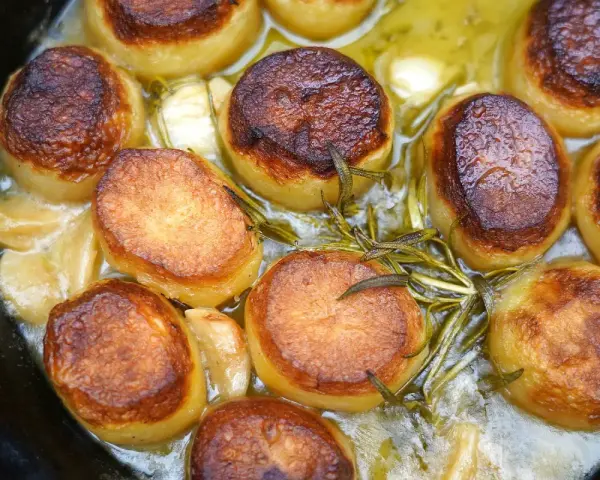 Saftige Fondant Kartoffeln mit Rosmarin und Knoblauch in einer Gusseisenpfanne, goldbraun gebraten.