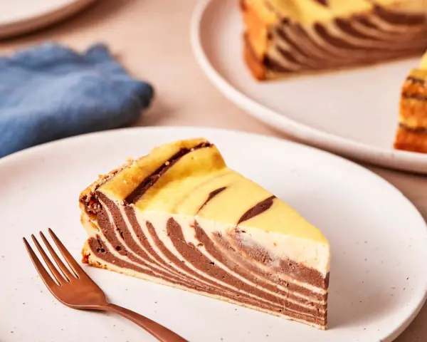 Ein Stück Zebrakuchen mit Quark, das auf einem Teller liegt, daneben eine Gabel.