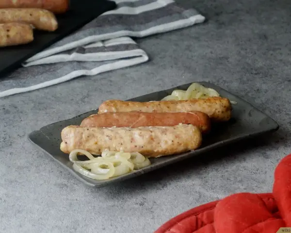 Drei Bratwürste mit Zwiebeln auf einem Teller, bereit zum Servieren. Sie sehen aus, als wären sie gerade aus dem Backofen gekommen.