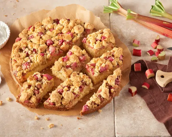 Ein saftiger Rhabarberkuchen mit Streuseln, perfekt für ein Rhabarberkuchen Rezept. Dazu eine Schüssel Schlagsahne.