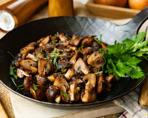 Gebratene Champignons in einer Pfanne, garniert mit frischer Petersilie. Ein köstliches Gericht, das zum Genießen einlädt.