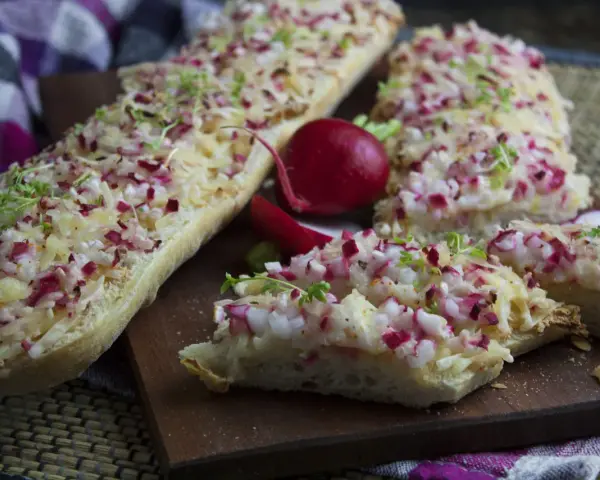 Baguette-Scheiben mit Radieschen und Käse belegt, eine köstliche Idee für Radieschen Rezepte. Frische Kresse garniert die Snacks.