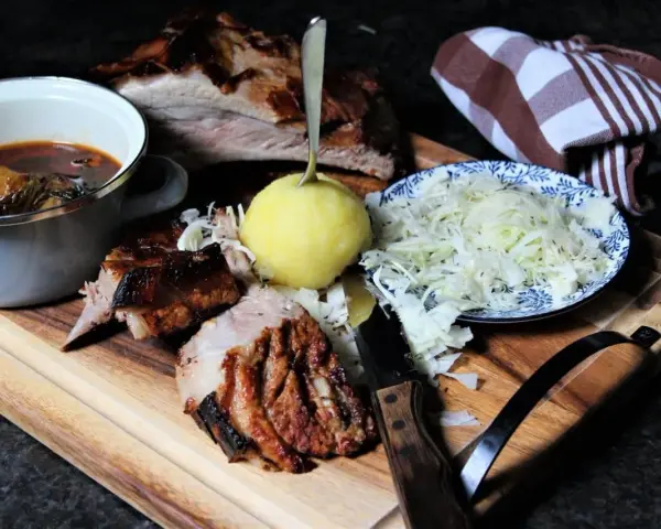 Deftige dicke Rippe mit Klößen, Sauerkraut und dunkler Soße auf Holzbrett.