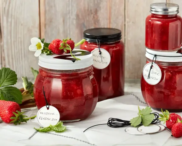 Gläser mit Erdbeer-Rhabarber-Marmelade, garniert mit frischen Erdbeeren und Blüten.
