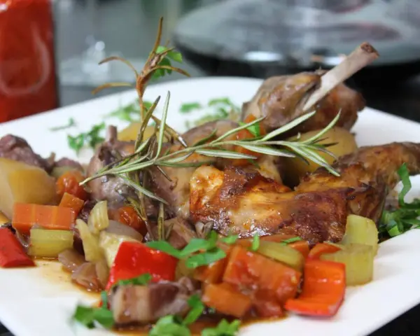 Klassisches Kaninchen-Rezept: Zartes Kaninchen mit Wurzelgemüse und Rosmarin auf einem weißen Teller serviert.