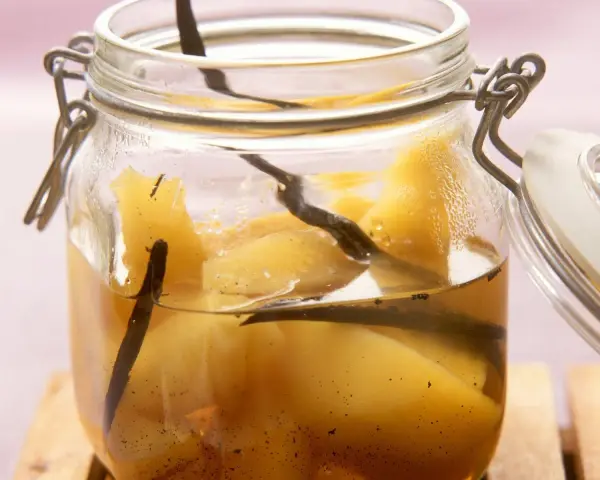 Ein Glas mit Quittenkompott, verfeinert mit Vanilleschoten. Die Fruchtstücke schimmern golden im Sirup.