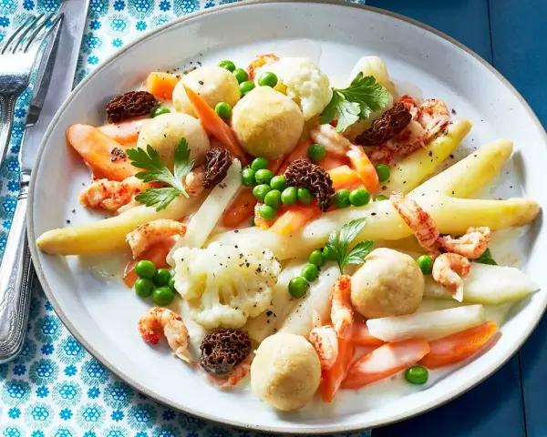 Leipziger Allerlei: Spargel, Erbsen, Karotten, Blumenkohl, Garnelen und Morcheln auf einem Teller.