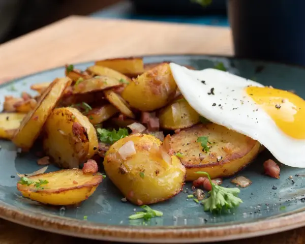 Bratkartoffeln mit Speck und einem Spiegelei, ein klassisches Rezept für ein herzhaftes Frühstück oder Abendessen.