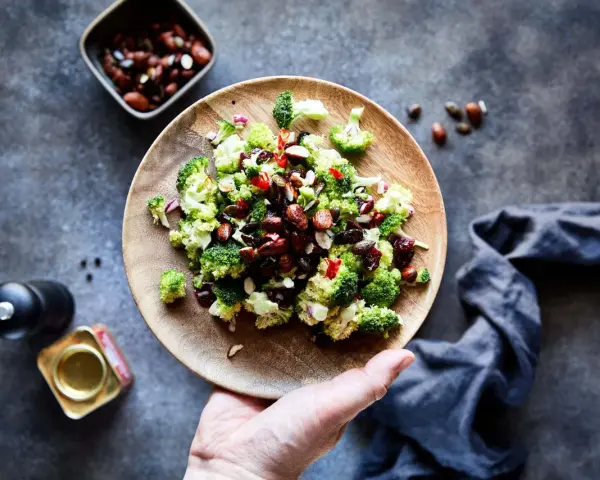 Frischer Brokkoli Salat mit Nüssen und roten Zwiebeln auf einem Holzteller, bereit zum Genießen.