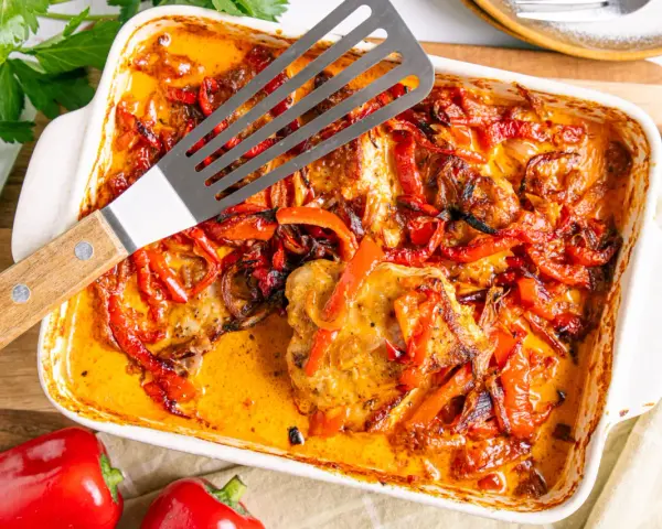 Herzhaftes Paprika Sahne Schnitzel in einer Auflaufform, mit roten Paprikastreifen und Zwiebeln in cremiger Sauce.
