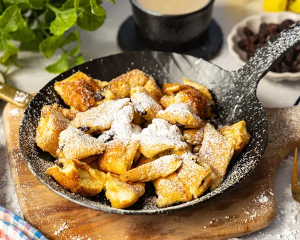 Ein fluffiger Kaiserschmarrn im Pfännchen, bestäubt mit Puderzucker. Perfekt für ein süßes Frühstück oder Dessert.