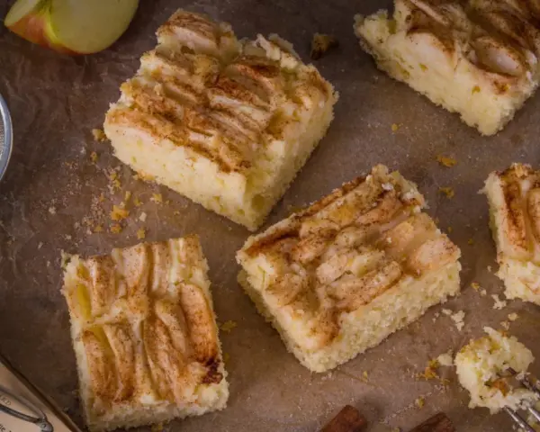 Saftige Apfel-Blechkuchen-Rezepte, bestreut mit Zimt. Ein Stück wird gerade mit einer Gabel probiert.