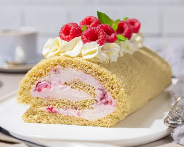 Himbeer Biskuitrolle mit Sahne und frischen Beeren, ein Genuss für jeden Kaffeetisch.