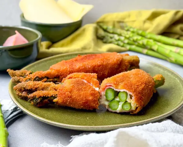 Knusprig paniertes Spargel Cordon Bleu mit Schinken und Käse gefüllt, auf einem grünen Teller angerichtet.