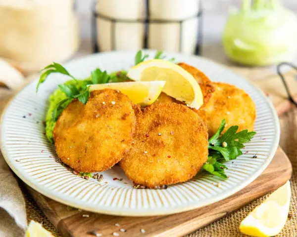 Knuspriges Kohlrabi Schnitzel auf einem Teller mit Erbsenpüree, Zitrone und Petersilie. Ein Genuss für Vegetarier!