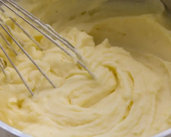 Cremiger kartoffelbrei ohne butter wird mit einem Schneebesen in einem Topf zubereitet.
