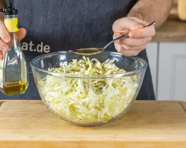 Ein Löffel Öl wird über den fein geschnittenen Spitzkohl gegeben, der für Omas Spitzkohlsalat vorbereitet wird.