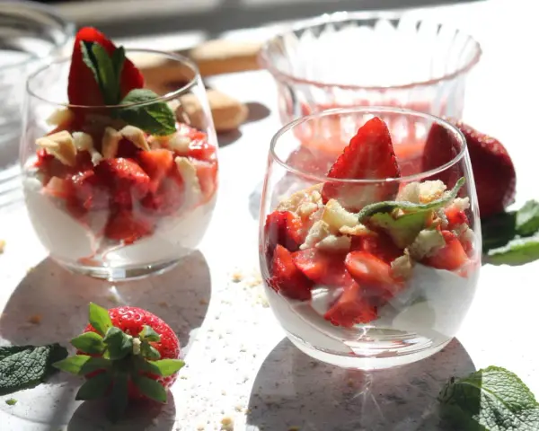 Zwei Gläser mit einem leichten Erdbeer Quark Dessert, garniert mit frischen Erdbeeren und Minze.