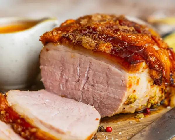 Saftiger Braten mit knuspriger Kruste, perfekt für die Zubereitung von Prager Schinken im Backofen. Dazu eine Schüssel mit Sauce.