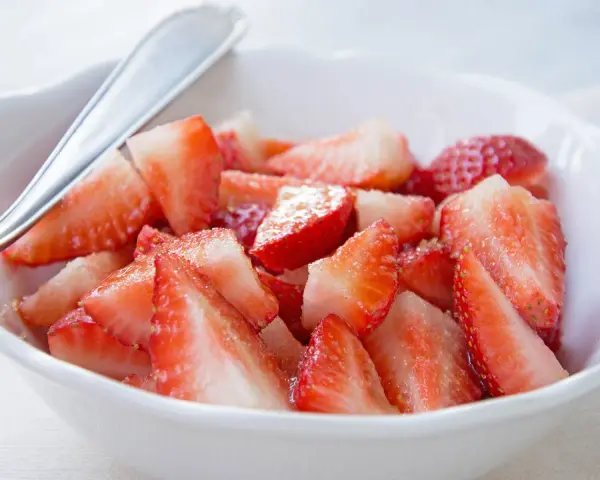 Schüssel mit marinierten Erdbeeren, die mit einem Löffel serviert werden. Saftige, rote Erdbeerstücke glänzen im Licht.