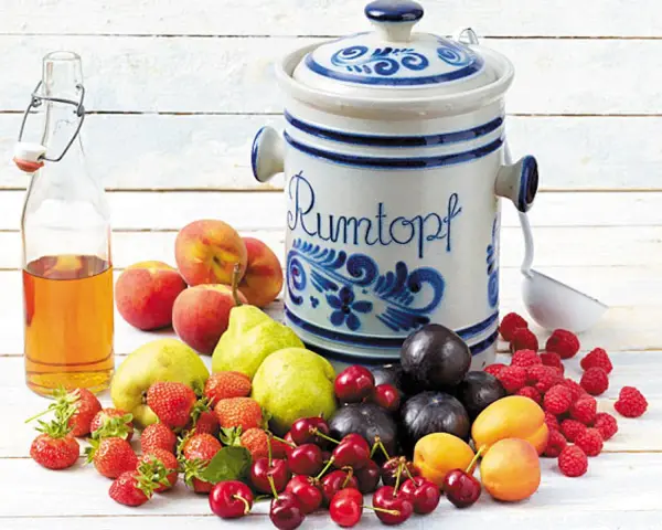 Früchte für ein Rumtopf Rezept nach Oma: Erdbeeren, Kirschen, Aprikosen, Pflaumen, Pfirsiche, Birnen, Himbeeren und eine Flasche Schnaps.