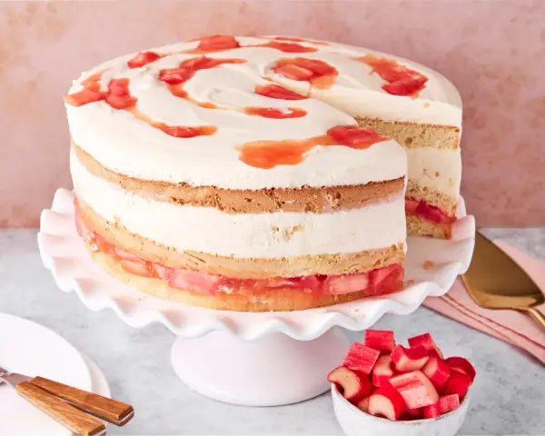 Eine köstliche Erdbeer Rhabarber Torte mit Sahne und Fruchtstücken, auf einem rosa Tortenständer präsentiert.