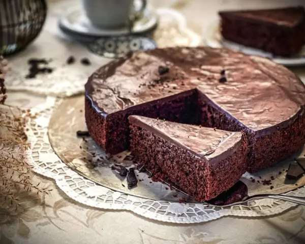 Ein saftiger Schokoladenkuchen mit glänzender Glasur, ein Stück wurde herausgeschnitten. Der einfache Kuchenteig sieht köstlich aus.