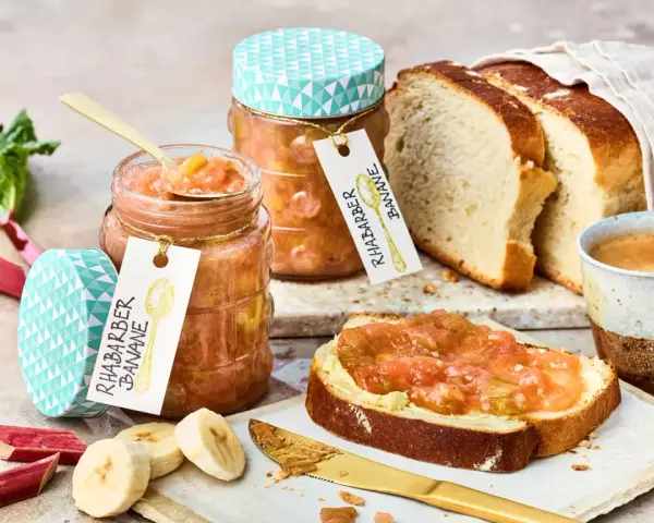 Zwei Gläser Rhabarber Bananen Marmelade, frischer Rhabarber, Bananenscheiben, Brot und Kaffee.