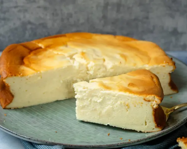 Ein saftiger Quarkkuchen ohne Boden, goldbraun gebacken, liegt auf einem Teller. Ein Stück ist bereits angeschnitten.