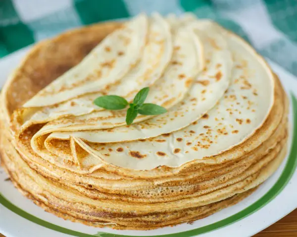 Ein Stapel goldbrauner Pfannkuchen, wie nach Omas Pfannkuchen Rezept gemacht, mit einem Minzblatt garniert.