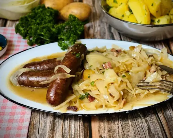 Deftige Bratwürste mit Zwiebeln auf bayrisch Kraut, garniert mit Petersilie. Dazu Salzkartoffeln und Senf.