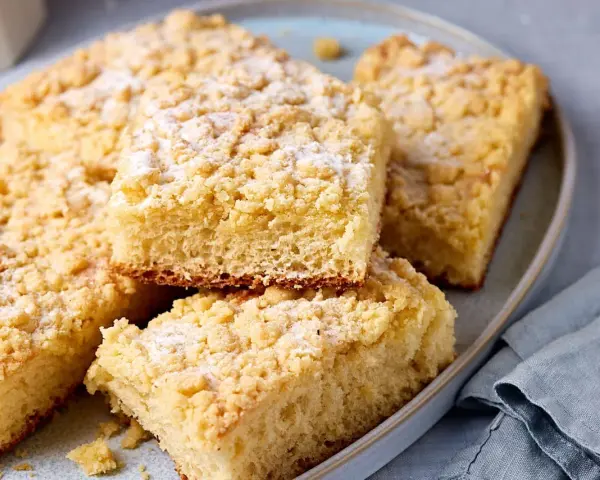 Saftiger Streuselkuchen vom Blech, mit Puderzucker bestäubt, liegt auf einem Teller.