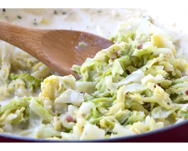 Cremiger Wirsing mit Speck, zubereitet mit einem Holzlöffel. Ein leckeres Gericht, das Lust auf mehr wirsing rezepte macht.