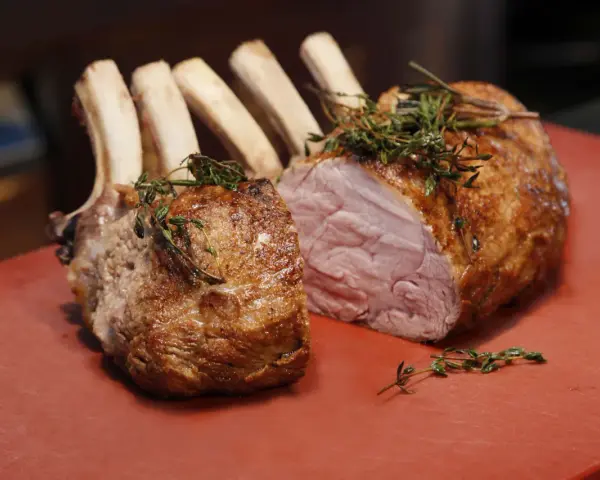 Ein gebratener Semerrolle Kalb mit Kräutern auf rotem Untergrund.