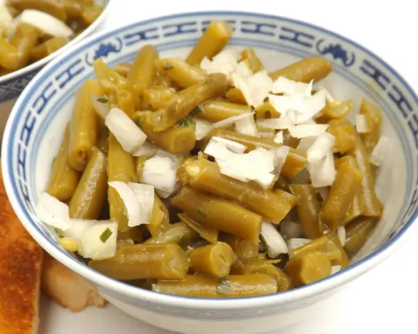 Bohnensalat rezept: Grüne Bohnen mit Zwiebeln in einer Schüssel, daneben geröstetes Brot.
