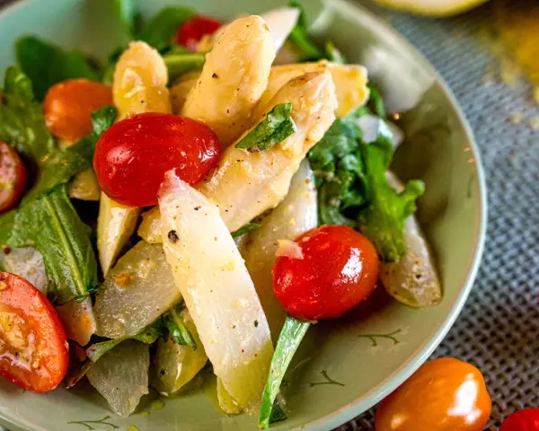 Ein Teller mit weltbestem Spargelsalat, garniert mit Kirschtomaten und frischen Kräutern. Ein Genuss für Augen und Gaumen.