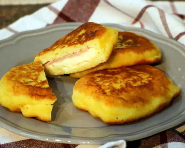 Goldbraune Kartoffel-Cordon-Bleu-Patties auf einem grauen Teller, gefüllt mit Schinken und Käse.