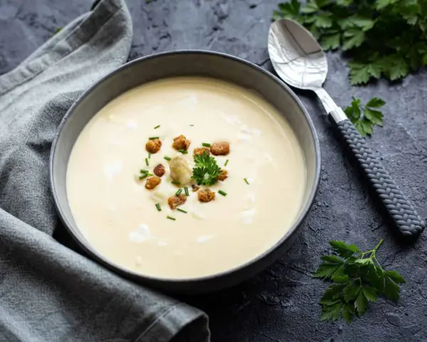 Cremige Spargelsuppe aus Schalen, garniert mit Croutons und frischen Kräutern. Ein Löffel liegt daneben.