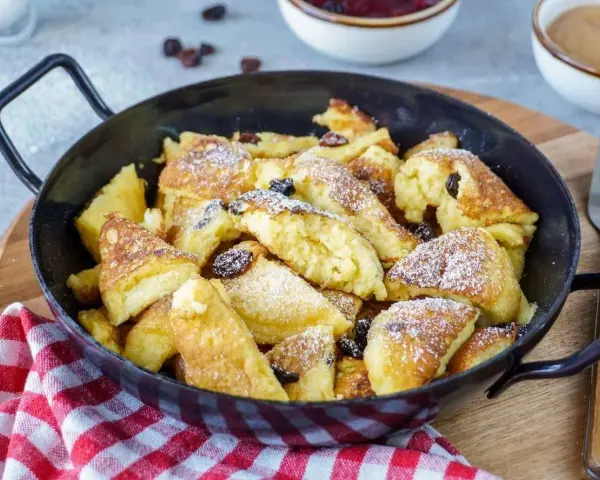 Leckerer, schneller Kaiserschmarrn im Backofen, bestäubt mit Puderzucker und Rosinen, serviert in einer Pfanne.