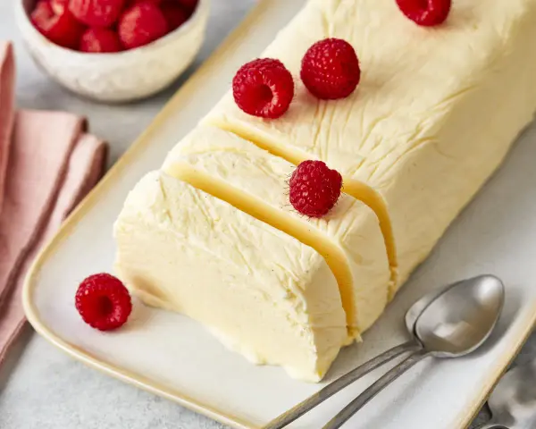 Cremiger Rhabarber Pudding, dekoriert mit frischen Himbeeren, auf einem Teller mit Löffeln.