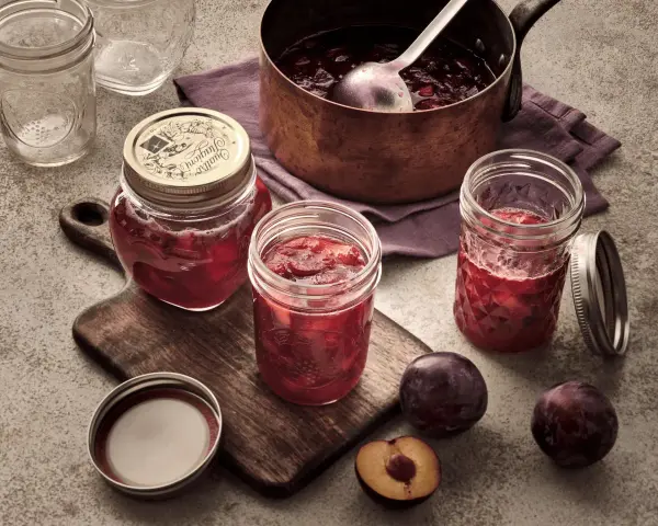 Frisch eingekochte Pflaumenmarmelade im Glas, bereit für das pflaumenmarmelade rezept. Frische Pflaumen liegen daneben.