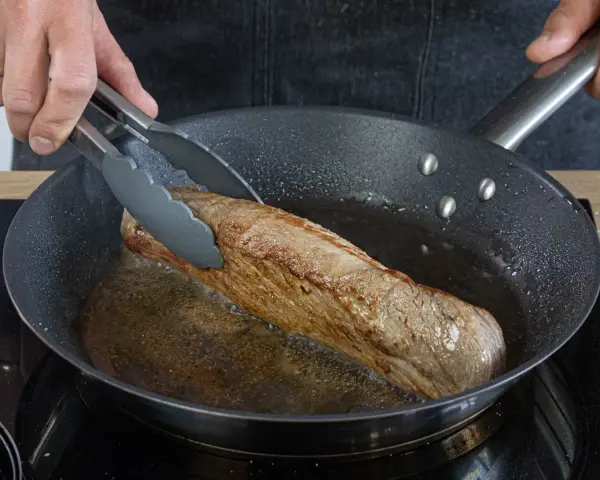 Ein saftiges Schweinefilet brät in der Pfanne. Einfache Rezepte für zartes Fleisch in der Pfanne gelingen so.