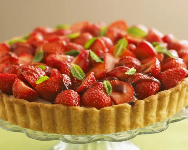 Ein köstlicher Erdbeerkuchen ohne Pudding, üppig belegt mit frischen Erdbeeren und Minze, auf einem Tortenständer.