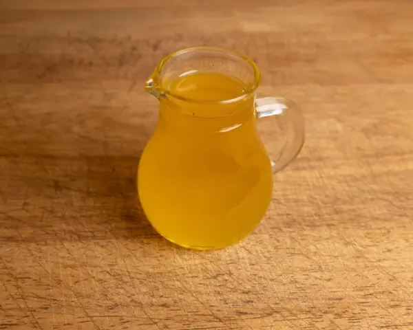 Ein kleines Glas mit goldgelbem Butterschmalz steht auf einem Holzbrett. Perfekt zum butterschmalz selber machen.