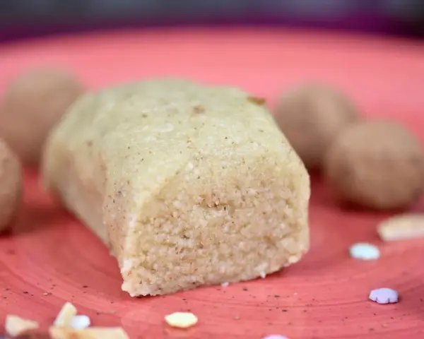 Ein Block selbstgemachtes Marzipan, ohne Rosenwasser, liegt auf einer roten Platte. Daneben sind Pralinen und bunte Zuckerstreusel.